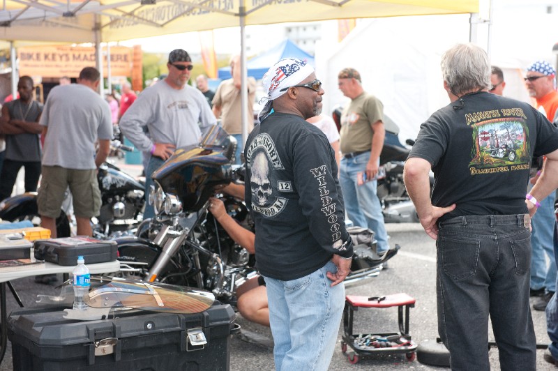 event attendees discuss motorcycle on display at vendor tent