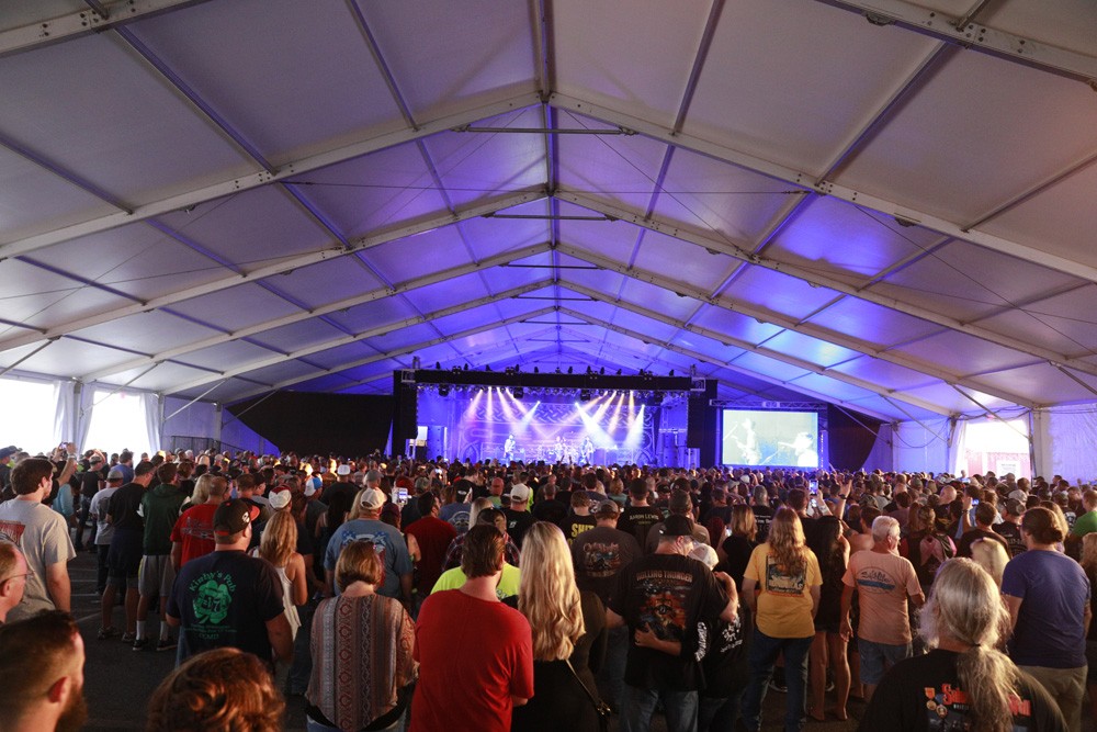 wide shot of large crowd watching rock band on stage under tent